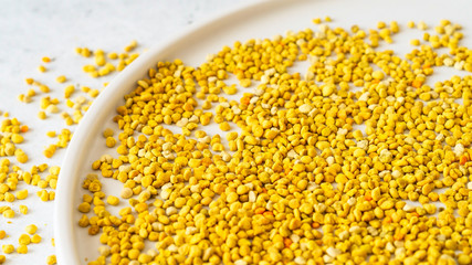 Bee pollen on white round plate on white stone background