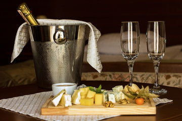 A bottle of champagne in a bucket with ice and glasses of champagne on a dark background. Festive theme with champagne still life, cheese plate, blur foreground