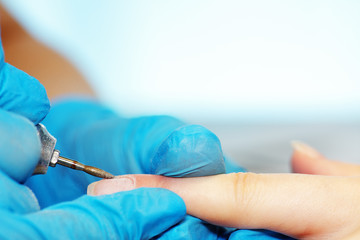 Closeup hardware manicure in a beauty salon. Manicurist use electric nail file drill to manicure on a female fingers.