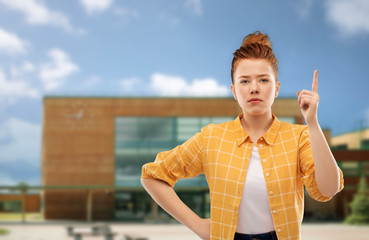 gesture, education and people concept - serious red haired teenage girl in checkered shirt pointing...