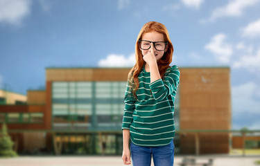 education, vision and childhood concept - smiling red haired student girl in glasses and green striped shirt over school background