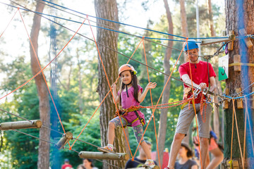Young father helping his little daughter in the rope park