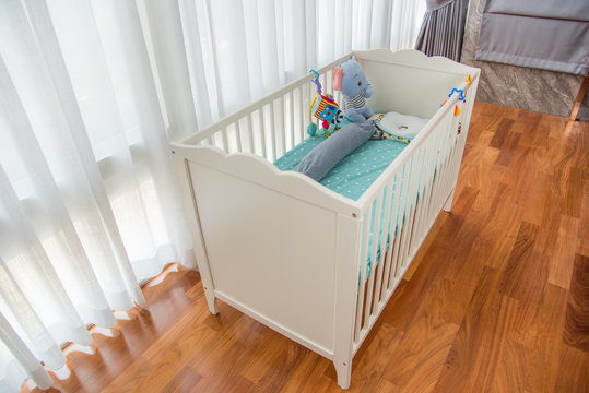 Children's wooden crib, painted in white with various soft toys and elephant in the cot on wooden floor room.