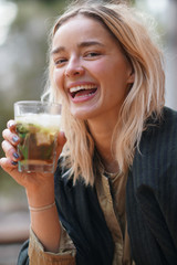 Cheerful young woman holding a cocktail grass outdoors