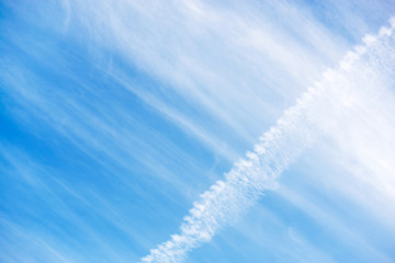 Beautiful light blue sky with white clouds and aircraft trail