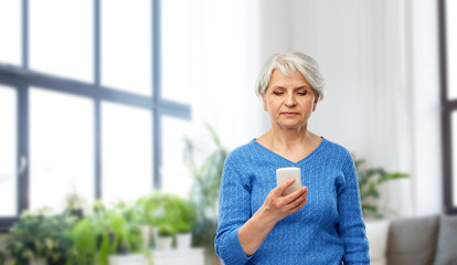 technology and old people concept - senior woman using smartphone over home living room background