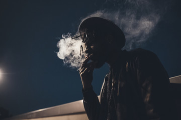 portrait of young black man standing outdoor smoking cigarette