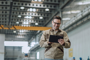 Portrait of a engineer working on tablet at large factory hall.