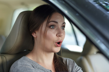 Fototapeta na wymiar Young attractive caucasian woman behind the wheel driving a car with grimace of astonishment or shock, mouth opened. Strong emotions, wow expression. Copy space.