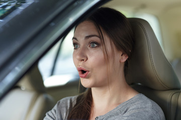 Fototapeta na wymiar Young attractive caucasian woman behind the wheel driving a car with grimace of astonishment or shock, mouth opened. Strong emotions, wow expression. Copy space.