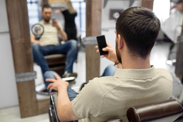 Fototapeta na wymiar grooming, technology and people concept - man with smartphone at barbershop or hair salon