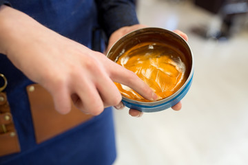 hairdressing and people concept - barber or hairstylist with hair styling wax at barbershop or salon