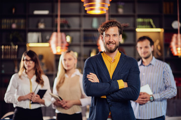 Smiling Caucasian businessman dressed smart causal standing in restaurant with arms crossed. In...