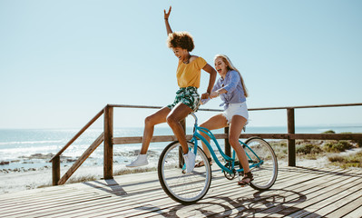 Female friends having fun on a bike at beach - Powered by Adobe