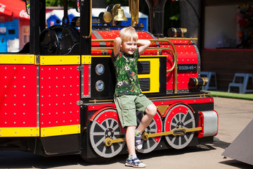 Little boy posing against the background of a steam locomotive in an amusement park