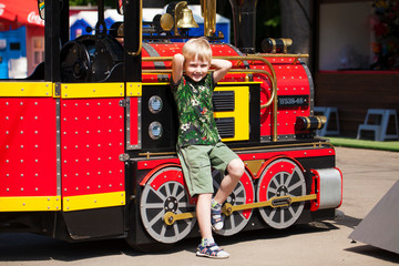 Little boy posing against the background of a steam locomotive in an amusement park