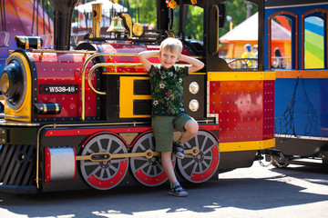 Little boy posing against the background of a steam locomotive in an amusement park