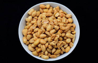 Salted fried peanuts on a plate with a blank black background.