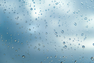 Raindrops on glass on clear sky background with clouds close up in summer