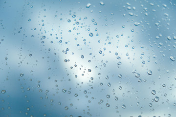 Transparent drops of rain on glass on background of clear blue sky with clouds closeup in summer