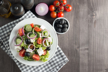 Fresh healthy salad with delicious ruccola, spinach, cabbage, arugula, feta cheese, red onion, cucumber, sesame seeds and cherry tomato on wooden background. Healthy and diet food concept.