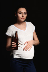 Pregnant woman with bottle of beer on dark background