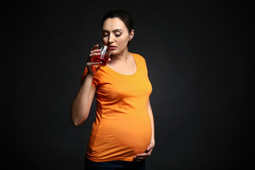 Pregnant woman with glass of alcohol on dark background
