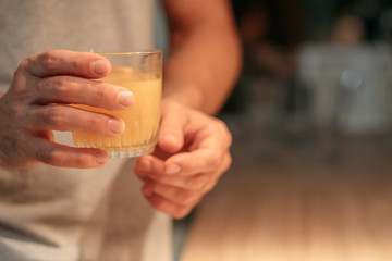 Vegan lifestyle. Cropped shot of man standing in kitchen with glass of fresh natural orange juice. Dark blur background.
