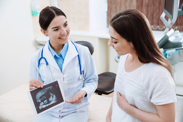 Female ultrasonographer working with pregnant woman in modern clinic