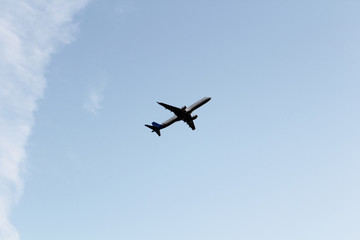 Plane on cloudy background. Airplane flying in clear pale blue sky.