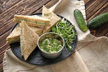 Plate with tasty cucumber sandwiches on wooden table