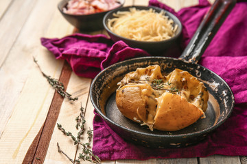 Frying pan with tasty stuffed potato on wooden table
