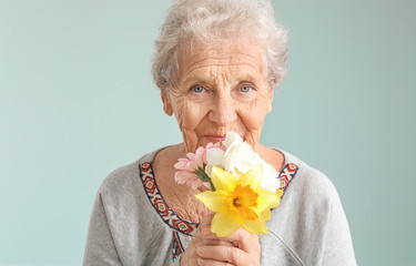 Portrait of senior woman with bouquet of flowers on grey background - obrazy, fototapety, plakaty
