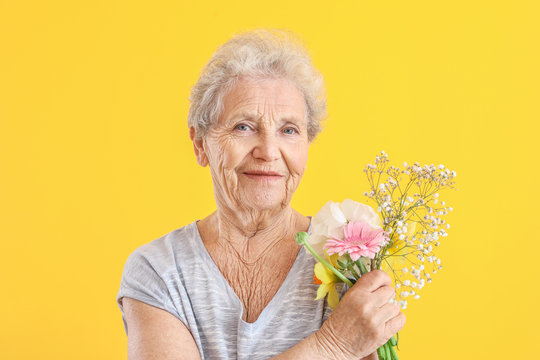 Portrait Of Senior Woman With Bouquet Of Flowers On Color Background