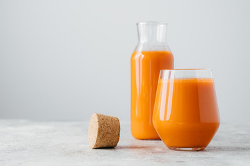 Fresh juice made of carrot filled in bottle and glass, cork near, isolated on white background, empty space. Detox drink. Healthy beverage