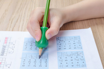 child's hand with writing tool for help by incorrect holding of pencil, homewortk, math