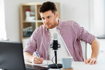 technology, mass media and podcast concept - male audio blogger with laptop computer, microphone and notebook broadcasting at home office
