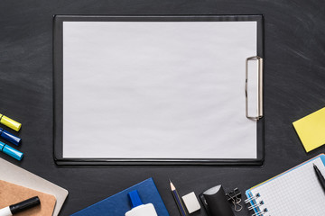 Education concept. Flat lay of blank mockup white sheet of paper on clipboard, school supplies over black chalkboard.