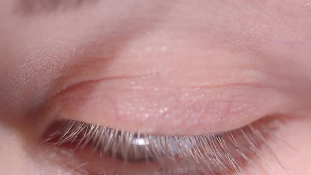 Close-up shoot of caucasian person with greenish eye blinks fastly and squints watching into camera.