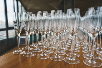 Several rows clear, clean glasses for wine and champagne on counter prepared for drinks.
