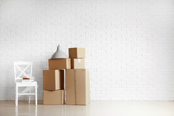 Cardboard boxes with belongings prepared for moving into new house near white brick wall