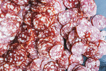 Thinly sliced sausage slices on a black stone board. 