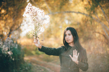 Dreamy beautiful girl with thistle flowers bouquet in golden sunlight on bokeh background with...