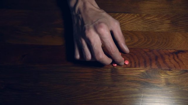 Hand of depressed man suffering from suicidal depression want to commit suicide by taking strong medicament drugs and pills playing with them with his hand on the wooden table health care concept 
