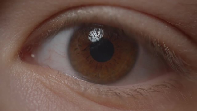 Close-up shoot of greenish eye with the reflection of lamp circling around.
