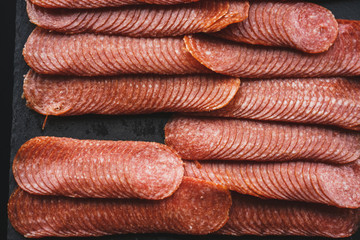 Thinly sliced sausage slices on a black stone board. 