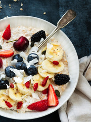 Bowl of oatmeal porridge with banana, blueberries, Goji berry, almonds, coconut and honey on teal rustic table, hot and healthy food for Breakfast. Superfood.