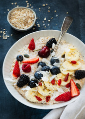 Bowl of oatmeal porridge with banana, blueberries, Goji berry, almonds, coconut and honey on teal rustic table, hot and healthy food for Breakfast. Superfood.
