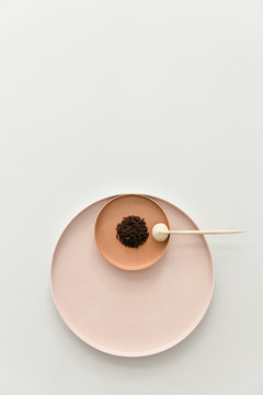 A batch of brown red rice layed out on a set of pastel powdery rose plates on a light grey table with a wooden spoon.