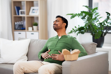 consumption and people concept - full and pleased indian man eating takeaway food at home